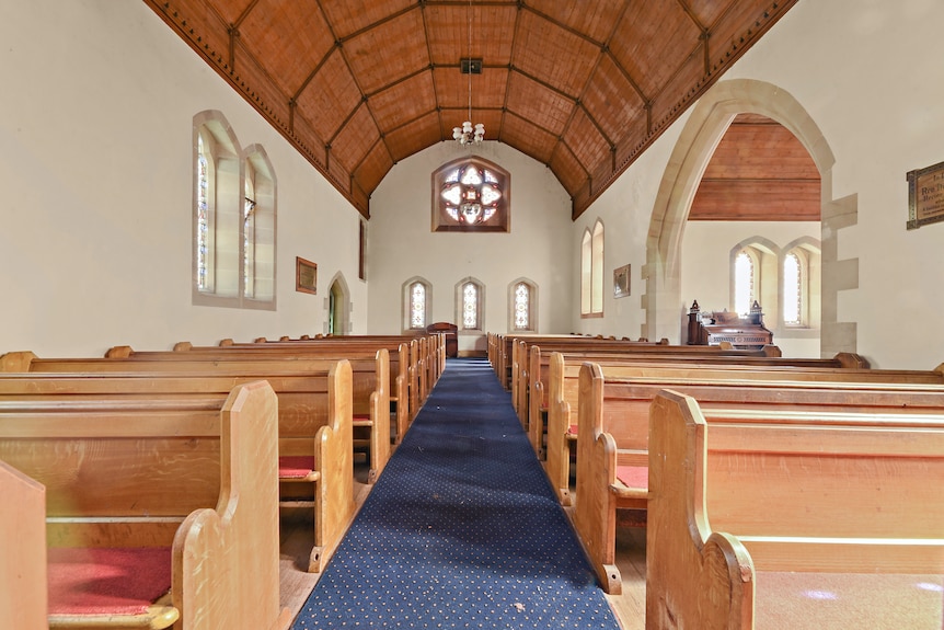 Rows of pews are seen in this interior shot of the church, along with a wooden roof and a stained-glass window. 
