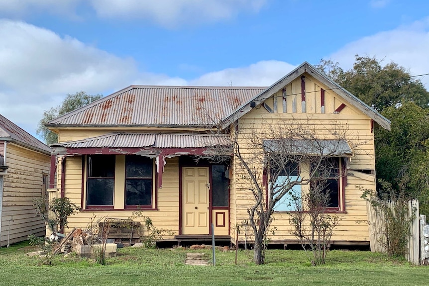 A yellow weatherboard house with a corrugated iron roof, in a state of disrepair.