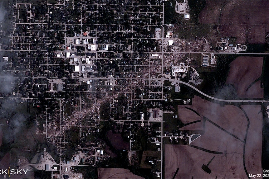 A black and white satellite photo of a small town arranged in a grid shows a trail of damage almost right through the middle.