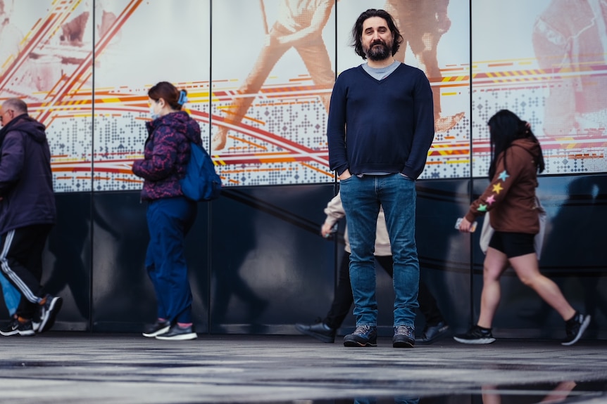 a man standing in front of a wall with his hands in is pockets