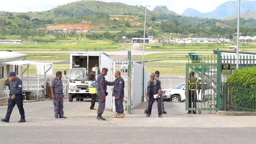 Men in police uniform stand near a gate with a truck in the background