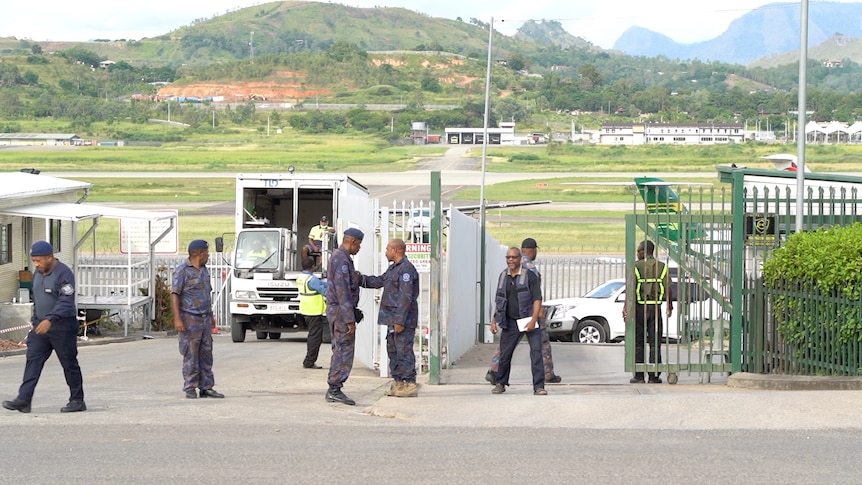 Men in police uniform stand near a gate with a truck in the background