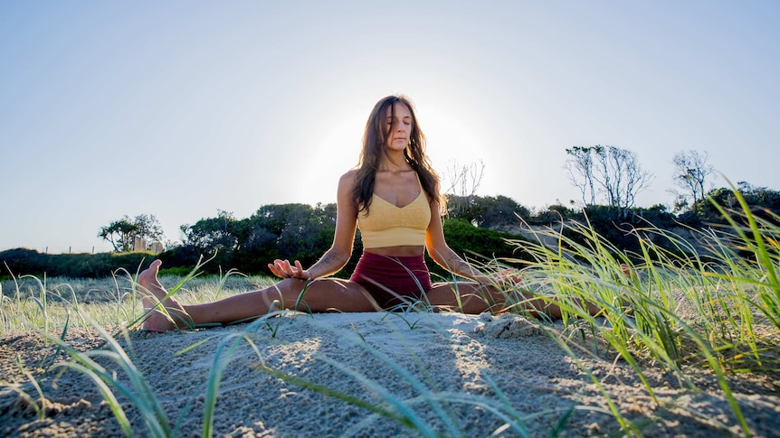 Lara, eyes closed and meditating in the sand dunes of Byron Bay