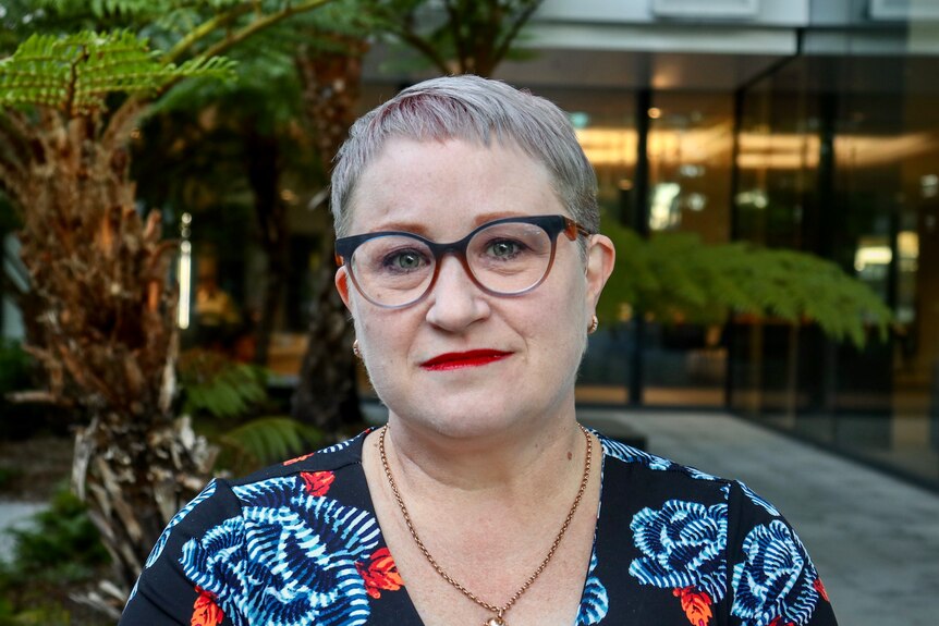 a woman with short grey hair wearing glasses and bright red lipstick looks directly at the camera