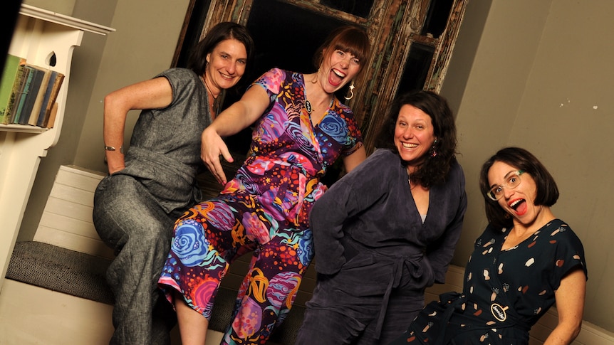 Four women wearing jumpsuits in identical designs but different fabrics smile at the camera.