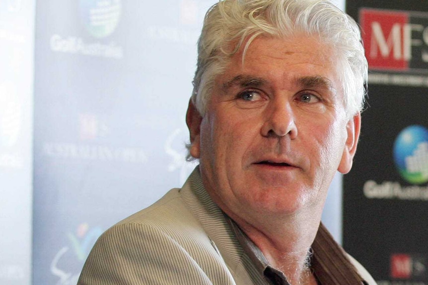 A headshot of Paul McNamee at a press conference in a light grey jacket.