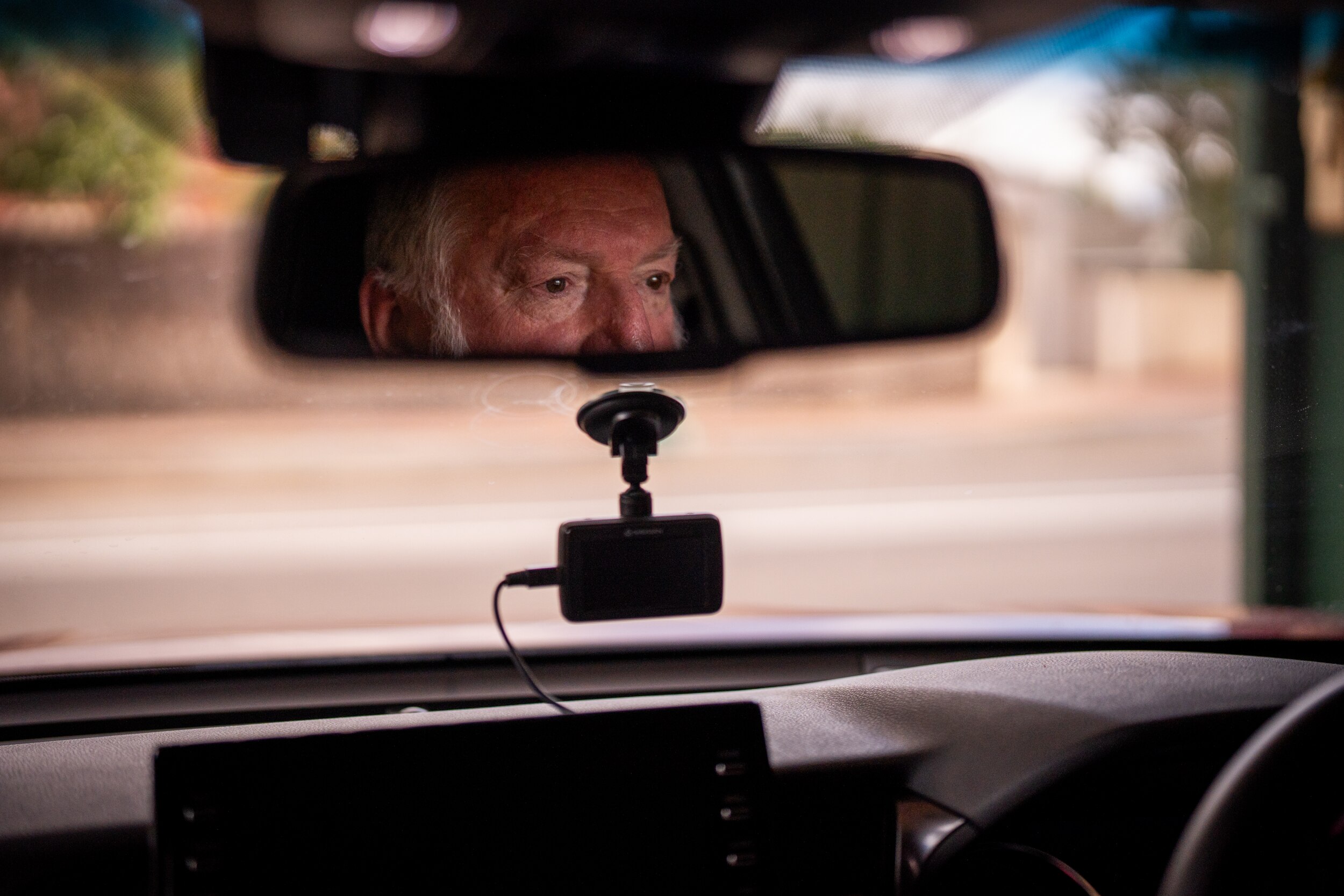 Allan Kelson's face can be seen in the rearview mirror as he sits in a car with a dashcam visible on his front window