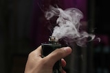 Hand holds vaping device with liquid vapour blowing out of it.