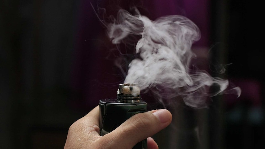 Hand holds vaping device with liquid vapour blowing out of it.