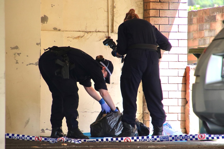 Two forensic police officers, one holding a camera, look into a rubbish bag. 