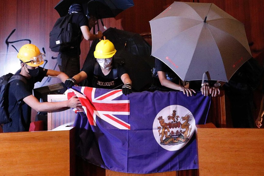 Protesters put a Hong Kong colonial flag and deface the Hong Kong logo at the Legislative Chamber.