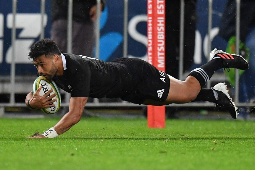A New Zealand All Blacks player dives holding the ball to score a try against the Wallabies in Sydney.