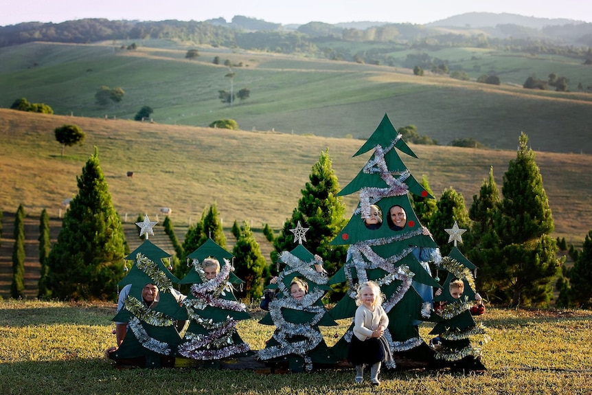 Photo of family standing behind life-sized cardboard Christmas trees on a pine farm