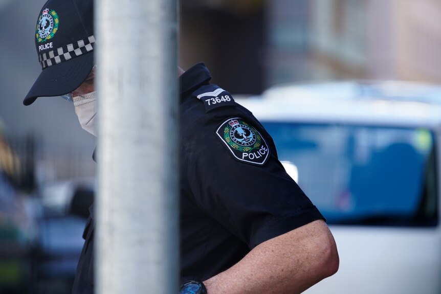 A policeman wearing a mask and cap stands behind a post