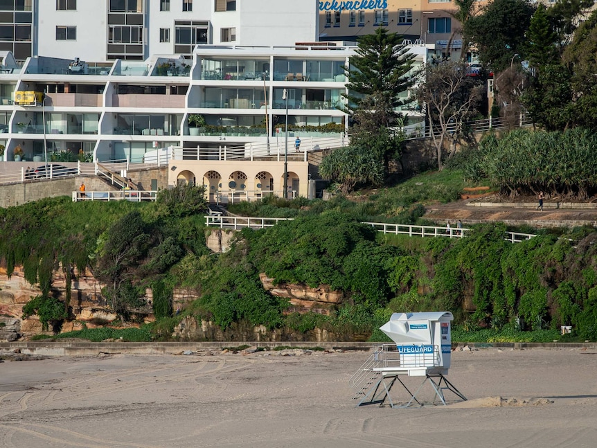 Empty sand and a closed lifeguard tower in front of a ramp where people walk and jog