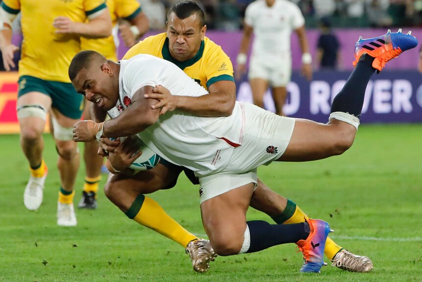 An England rugby player is tackled by an Australian opponent as he dives over the goal line to score a try.