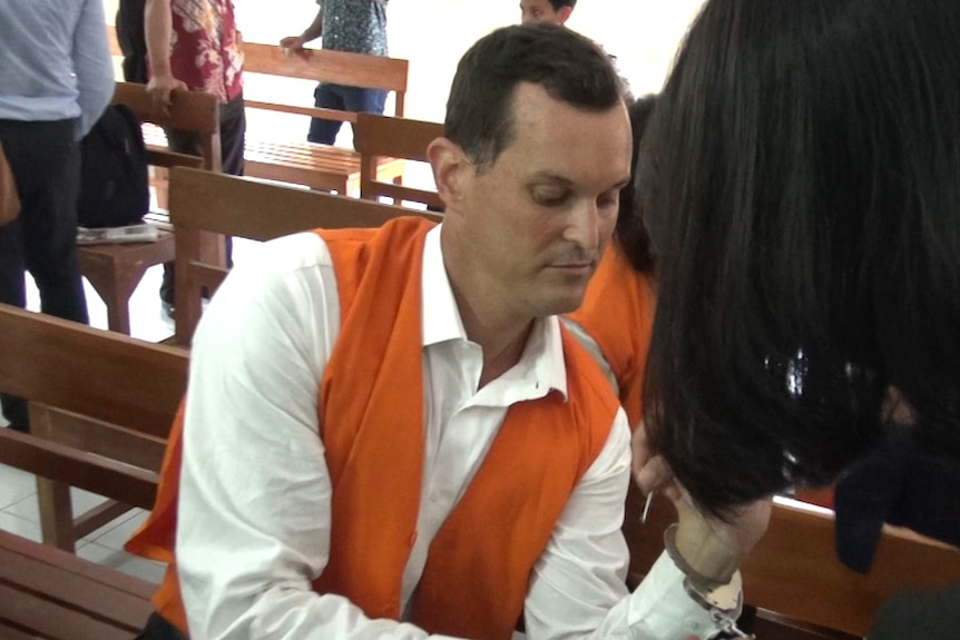 A woman uncuffs Mr Harmon in a courtroom.