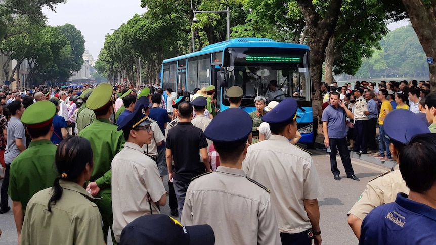 Polisi berdiri di sekitar bis setelah menahan beberapa pengunjuk rasa di Hanoi.