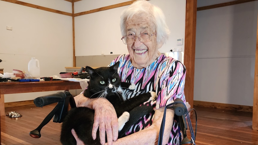 An elderly woman holding a black cat and smiling