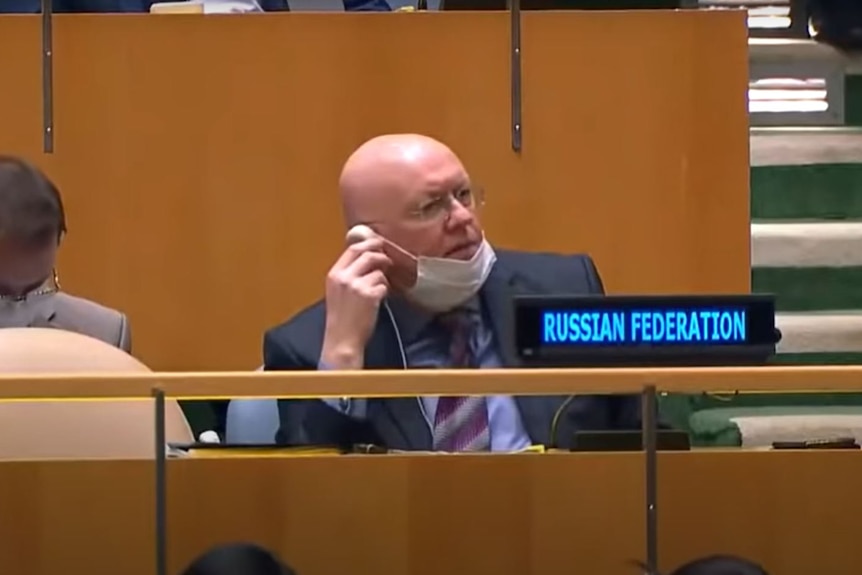  Vasily Nebenzya holds a speaker up to his ear with a serious expression on his face. 
