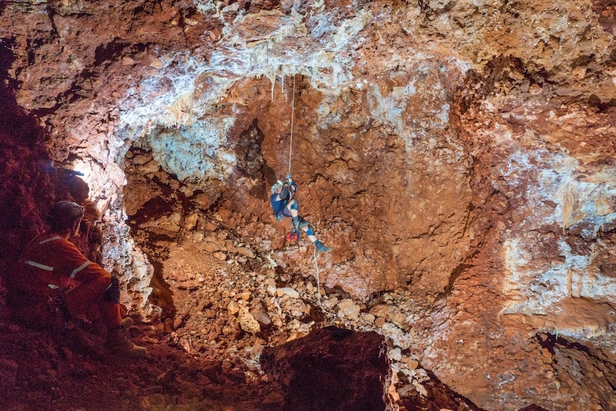 A man abseils in the void of a large cave chamber.