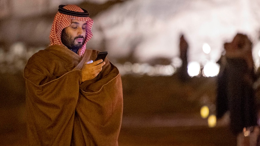 Saudi Arabia Crown Prince Mohammed Bin Salman stands alone, looking at his phone 