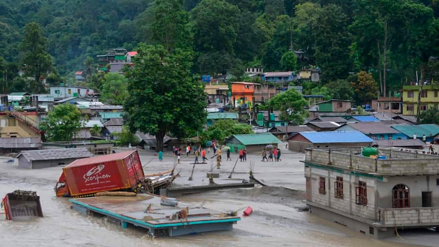 A wide shot of a village in India submerged in water, with infrastructure damaged. 