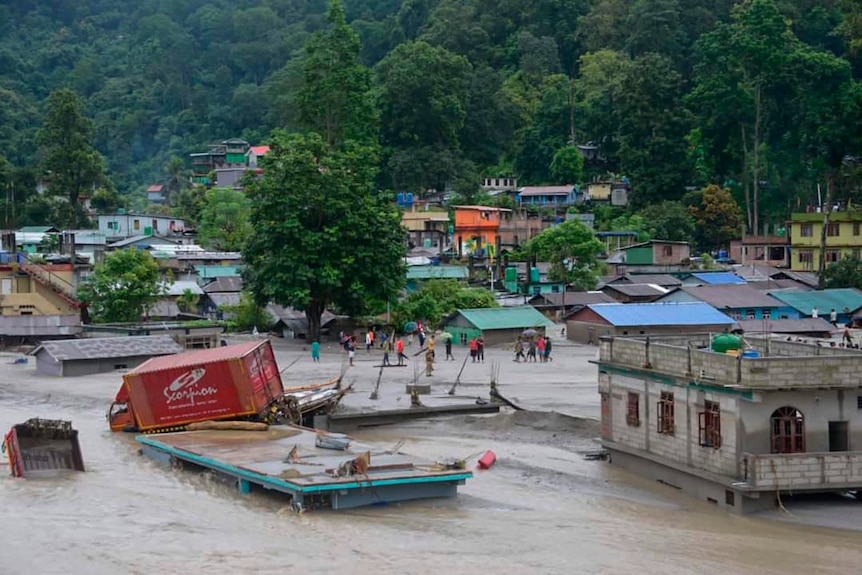 A wide shot of a village in India submerged in water, with infrastructure damaged. 