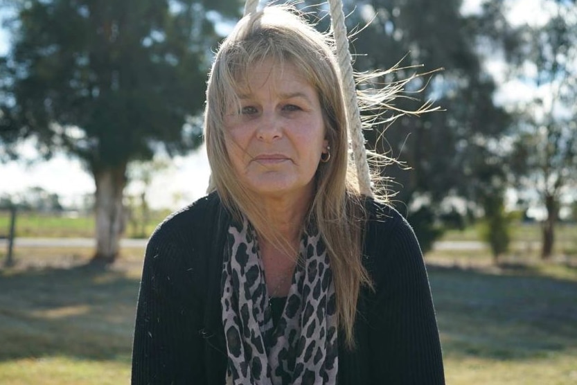 A woman sits on a swing in a playground looking downcast.