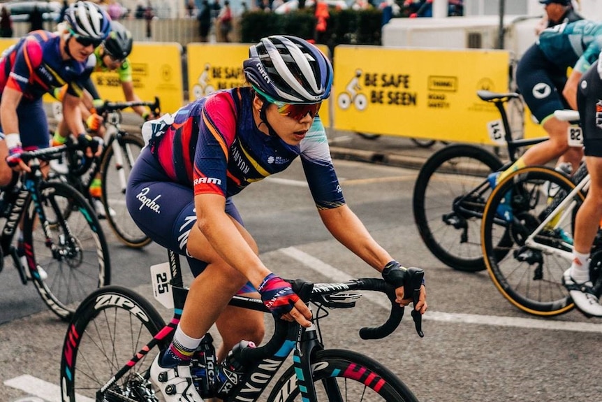 Wearing a blue and pink jersey, Jess Pratt has her eyes straight ahead while riding her bike