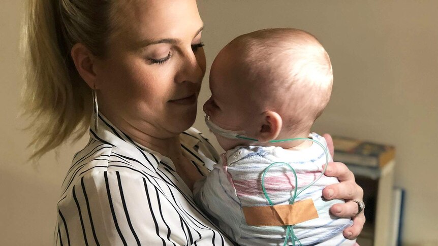 Mother holding 7-month old baby with tubes wrapped around his back into his nose.