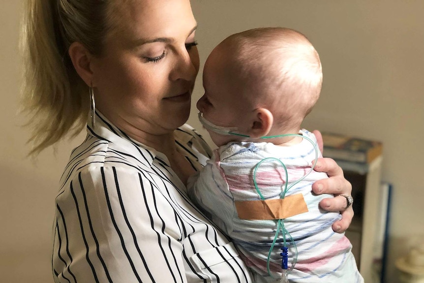 Mother holding 7-month old baby with tubes wrapped around his back into his nose.