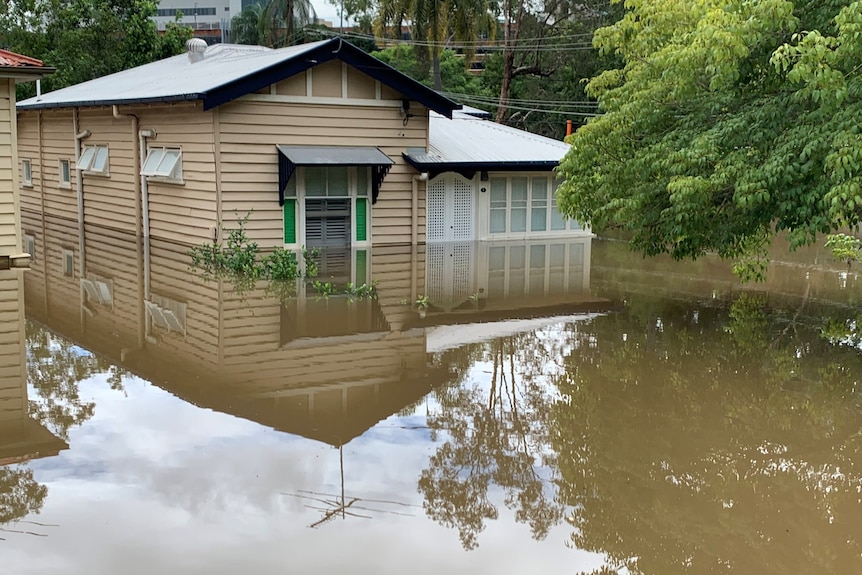 A house surrounded by brown water. Water half way up the front windows. 