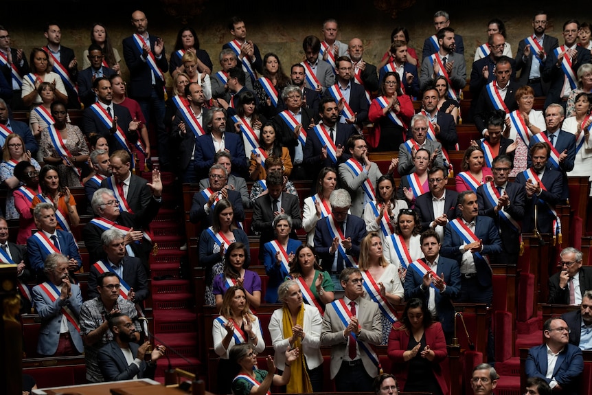 a large group of people in parliament wearing red, white and blue sashes