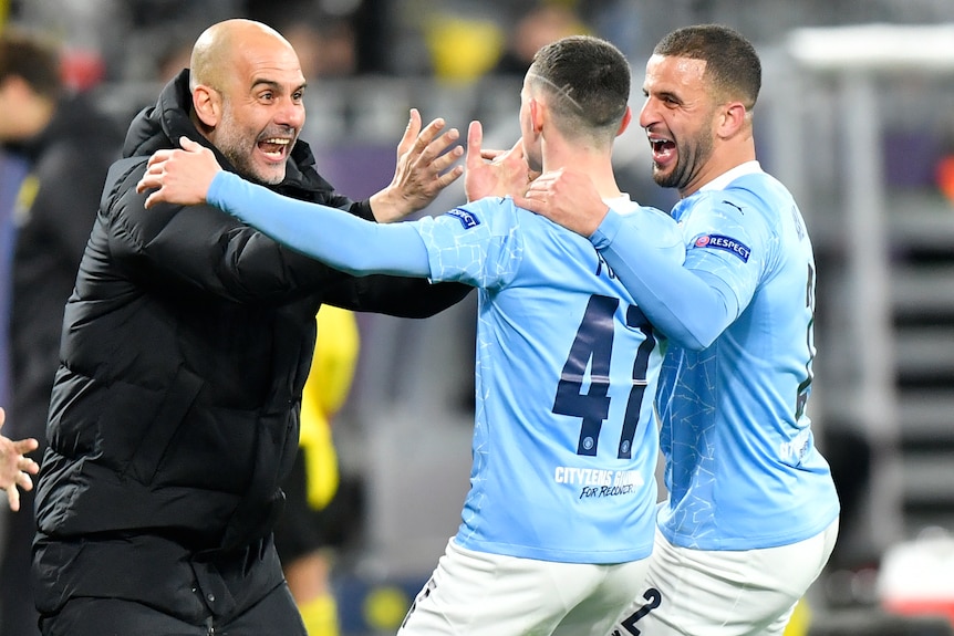 Pep Guardiola smiles and reaches for Phil Foden's face in celebration. Kyle Walker has his arm around Foden