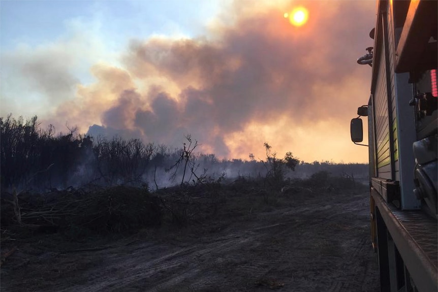 A fire truck next to burnt bushland and smoke as the sun comes up