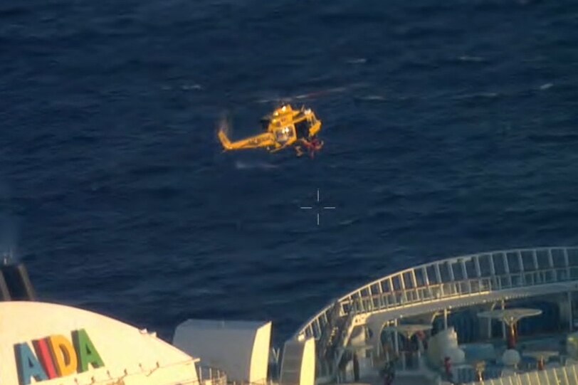 Yellow RAC chopper out at ocean, hovering over large cruise ship