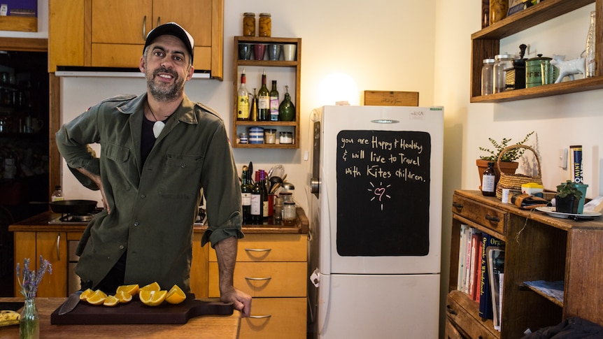 Camilo at home in his kitchen leaning on the bench.