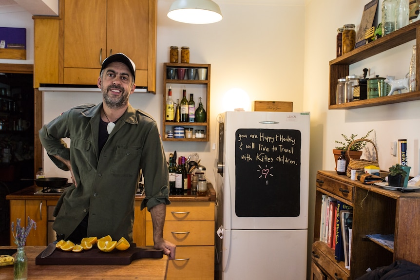 Camilo at home in his kitchen leaning on the bench.