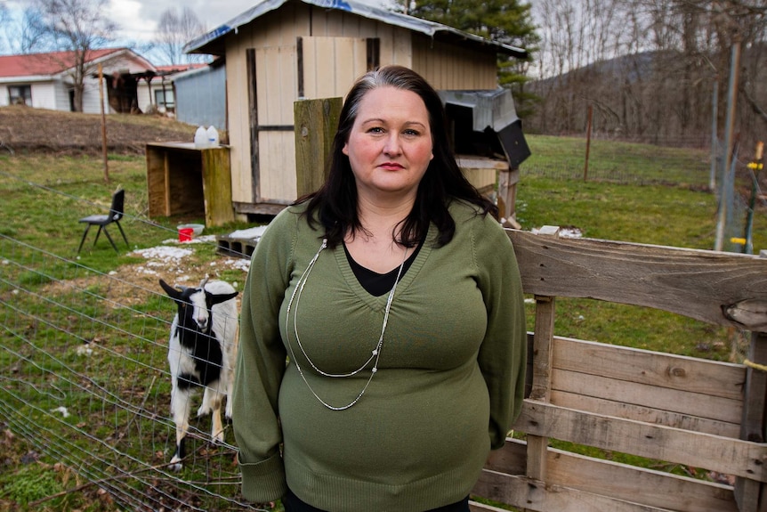 A woman standing in front of a fence with a goat behind her