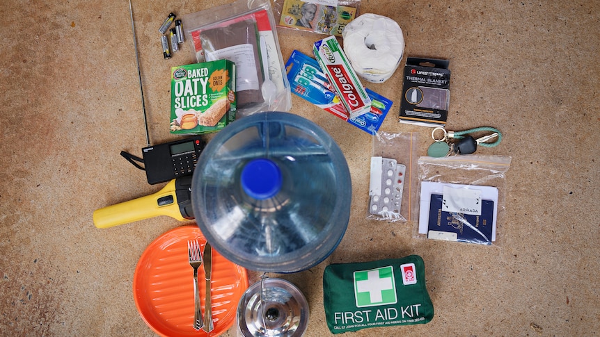 The contents of a cyclone kit are spread out on the ground. It includes water, a first air kit and toiletries.