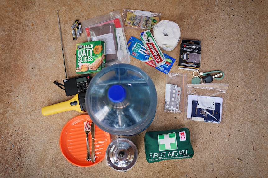 The contents of a cyclone kit are spread out on the ground. It includes water, a first air kit and toiletries.