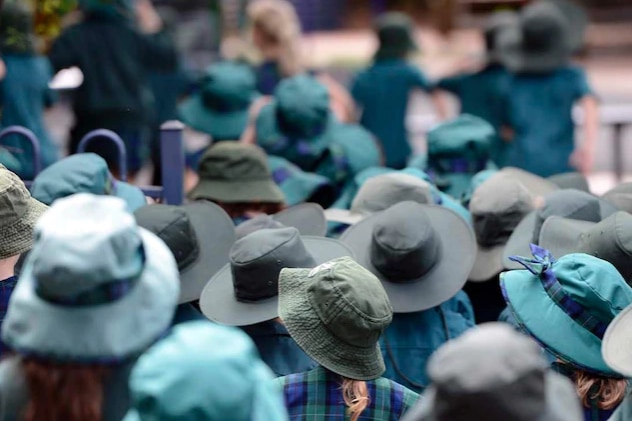 A dozen young school children standing outside with hats on.