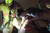 In a night-time scene, a firefighter carries a teenage boy out of the rubble of a collapsed building.