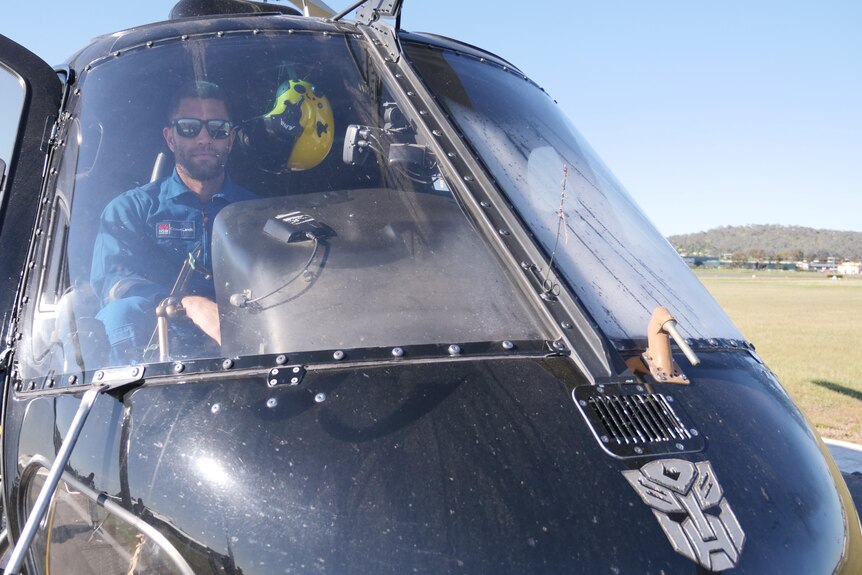man with sunglasses in blue shirt sits in helicopter cockpit with transformers sticker on front