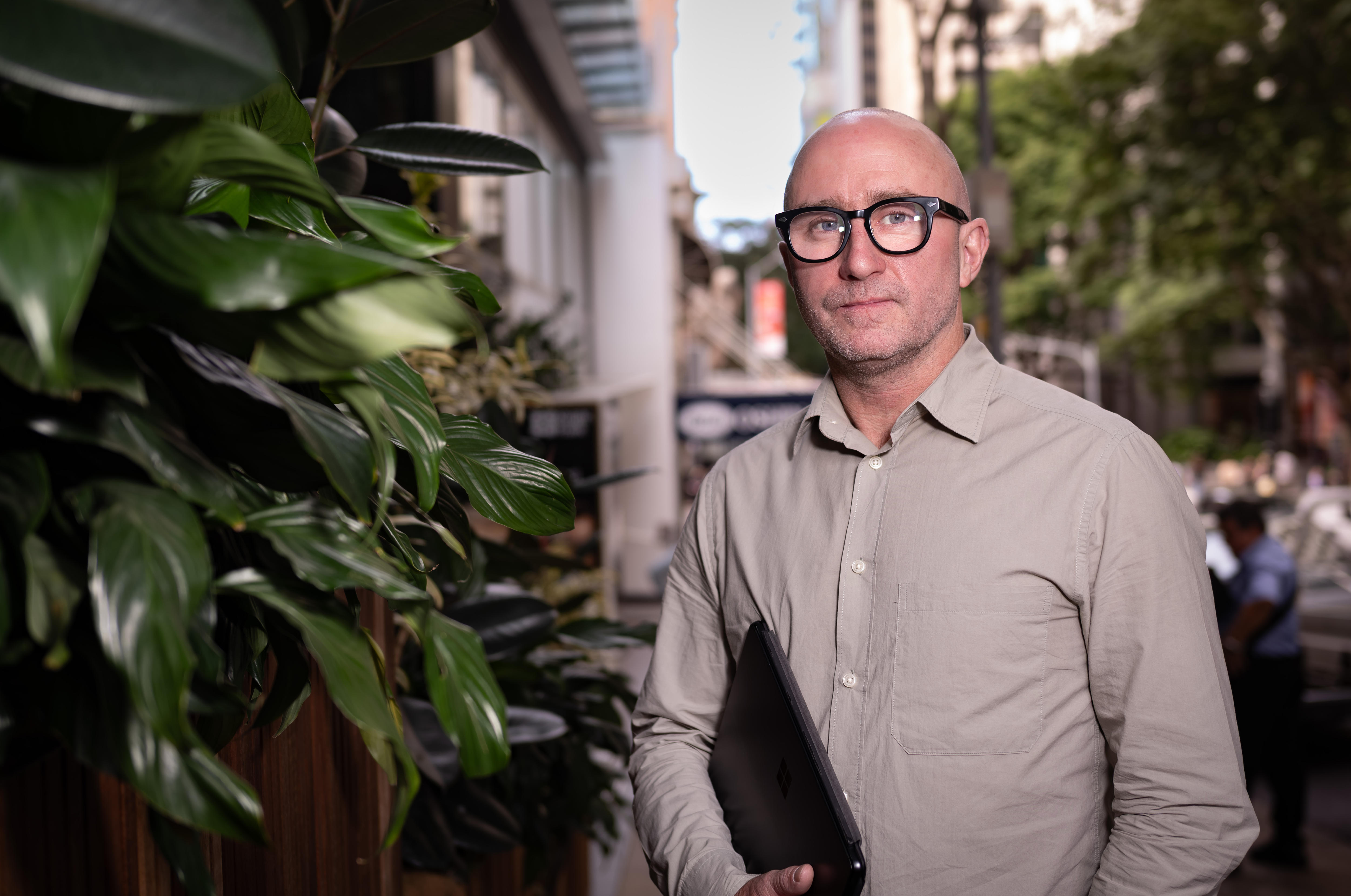Un hombre con gafas y la cabeza rapada se encuentra en una calle de la ciudad.