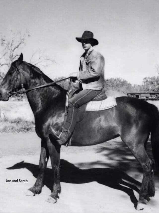  A black and white picture of a man in a cowboy hat riding a black horse.