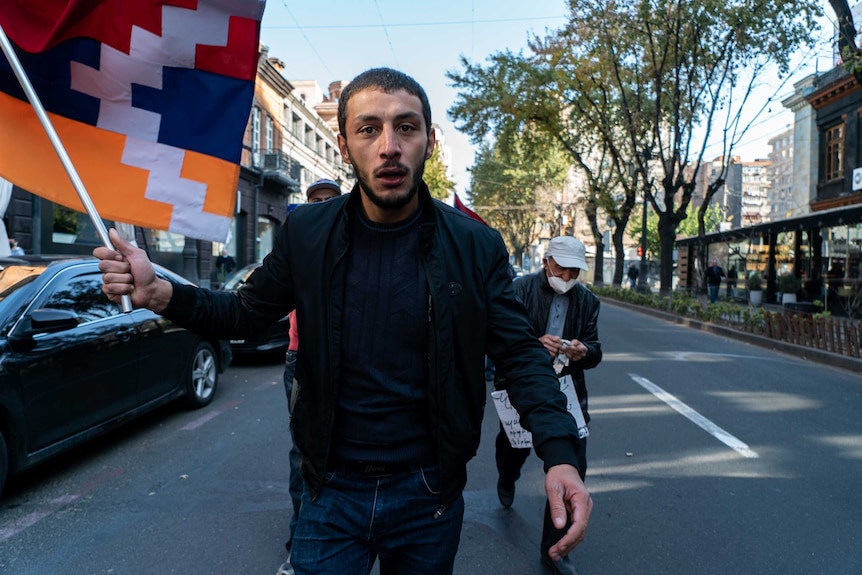 A man with an exhausted expression holds a flag and walks through the street