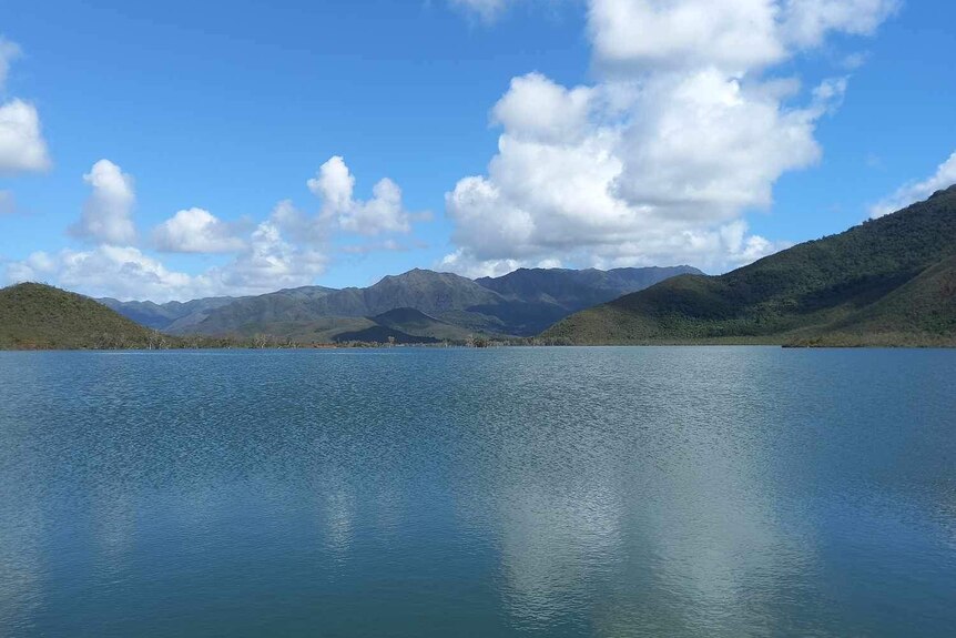 A lake with mountains in the background and blue sky with some clouds.