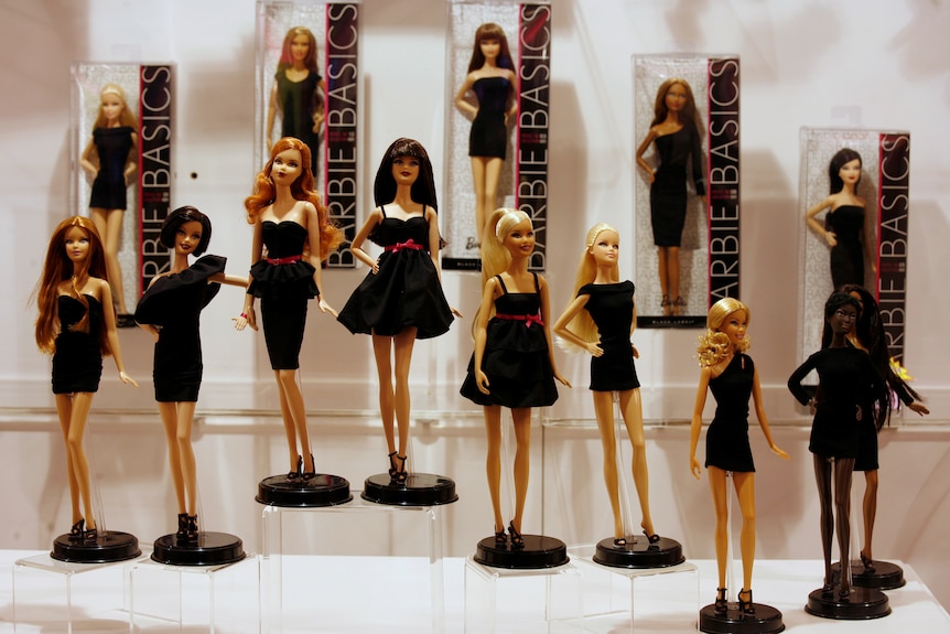 A dozen Barbie dolls on display, some blonde, black, red-haired